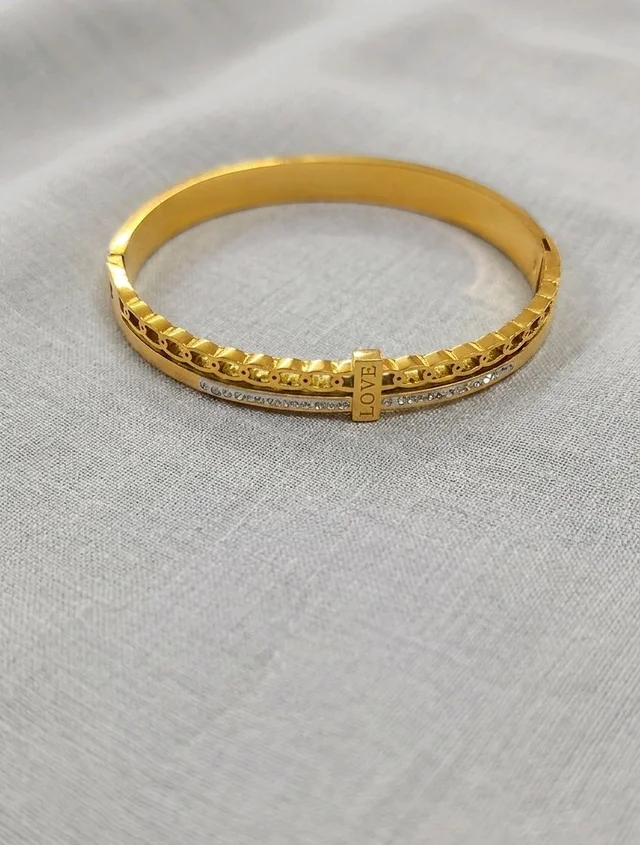Kada gold-toned fashion cuff bracelet featuring a textured design and a small bar engraved with the word "LOVE